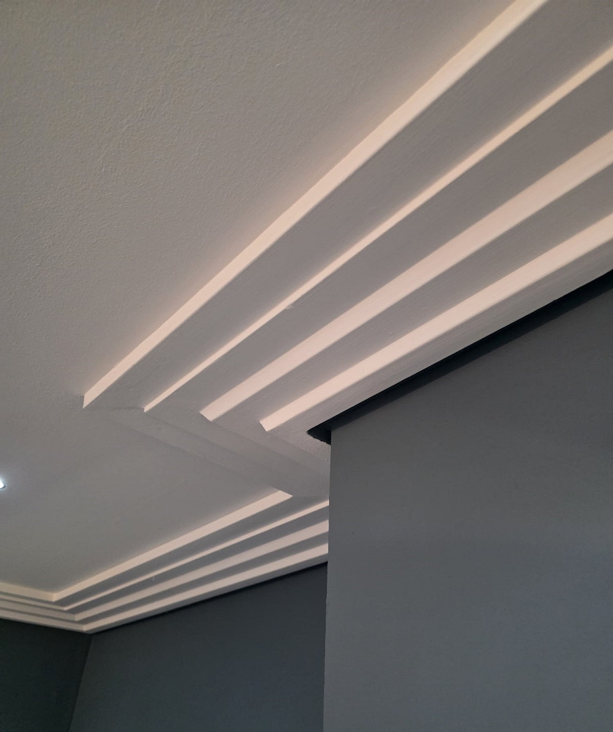Ceiling coving with recessed lighting and a corner of a room with a dark wall.