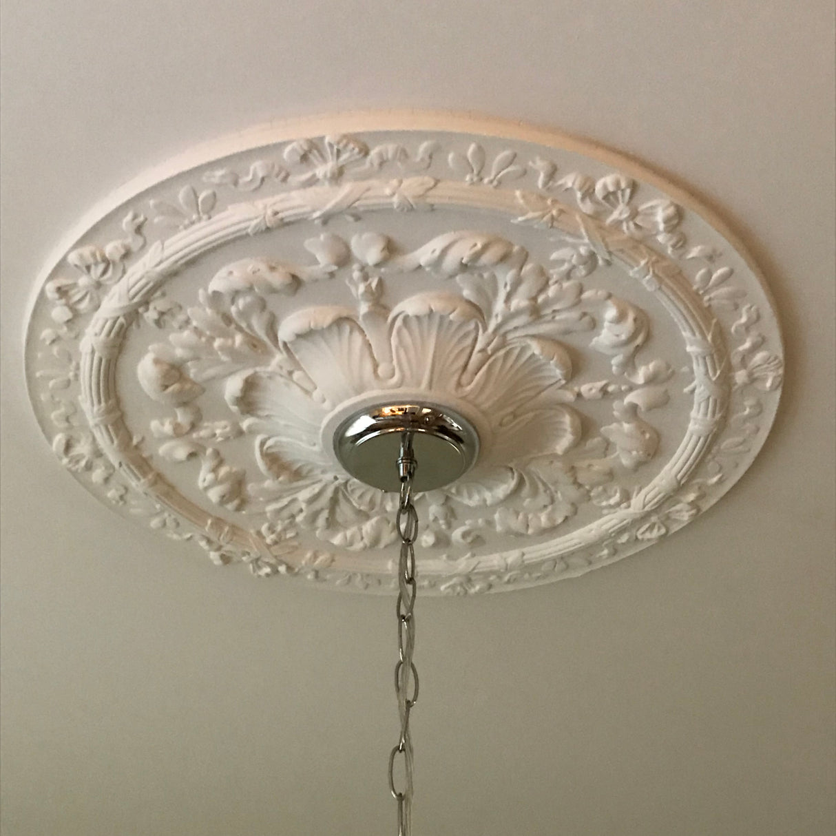 An Victorian ornate white decorative ceiling medallion with a floral relief pattern.